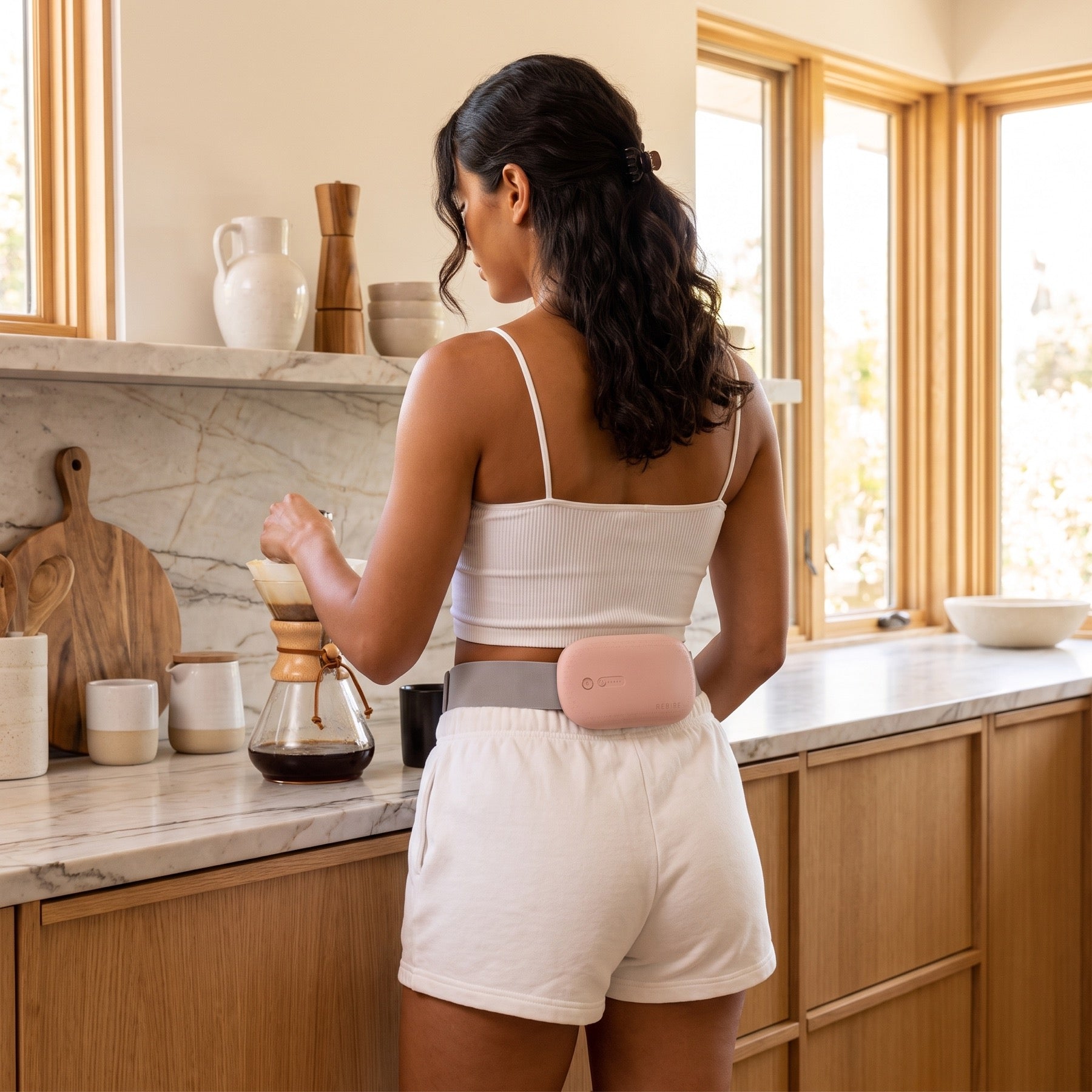 A woman making coffee at home, the NuFemme belt worn at her lower back