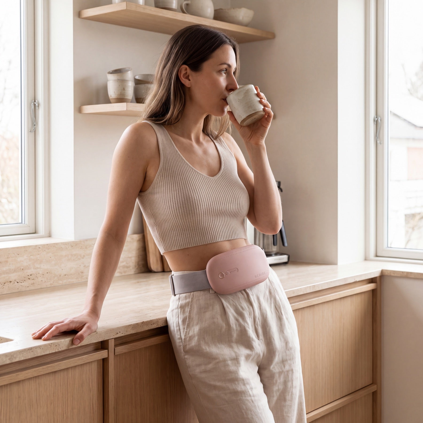 A woman standing in her kitchen with a coffee, the NuFemme belt at her waist